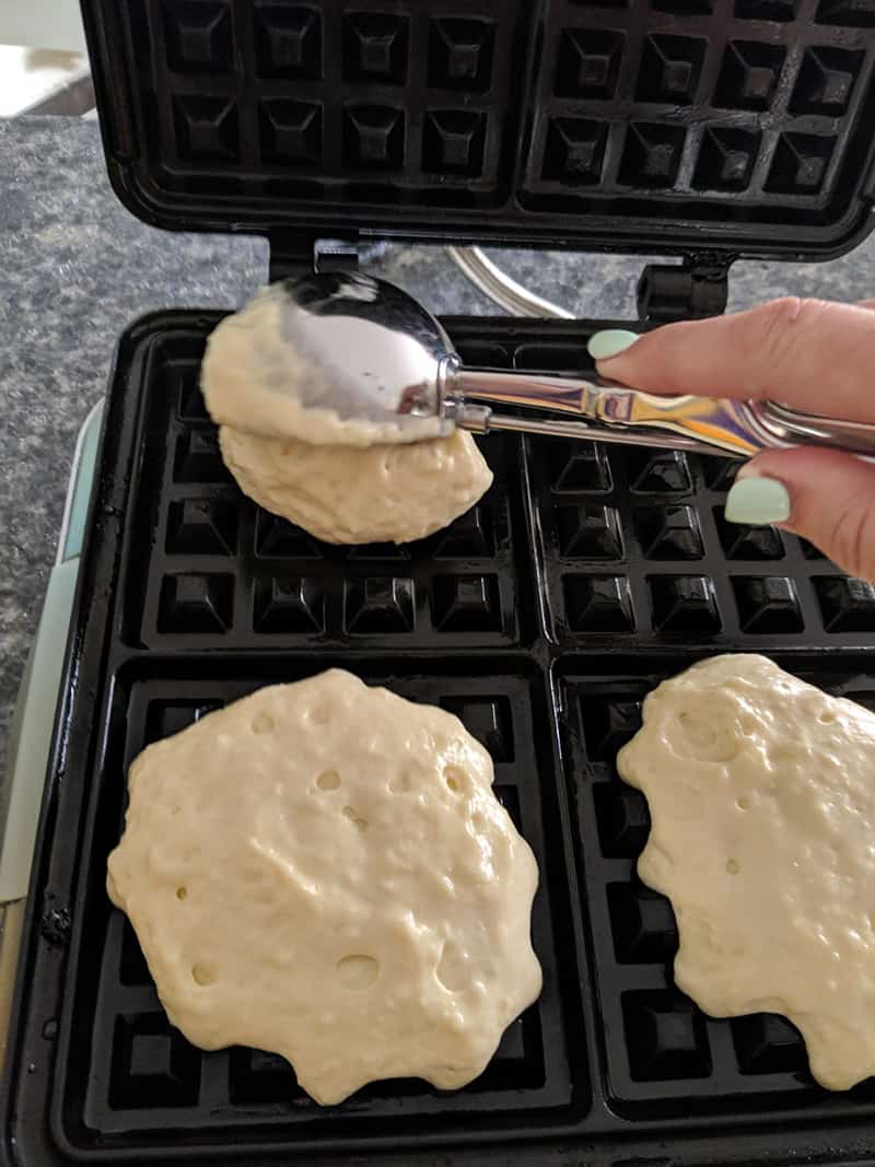 using a cookie scoop to scoop waffle batter onto a waffle maker