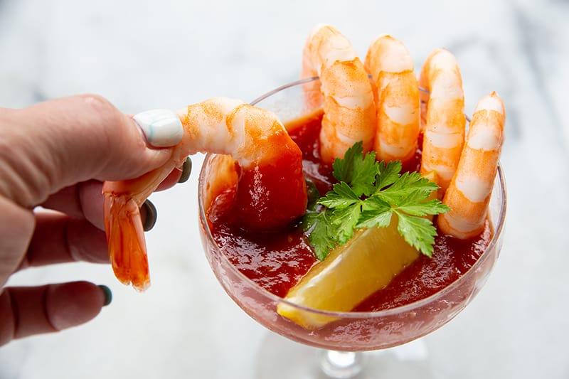 5 cocktail shrimp around a serving glass with Cocktail Sauce garnish with a slice of lemon and parsley leaves