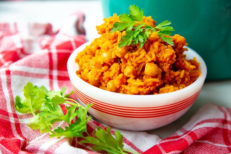 red checkered tablecloth underneath a bowl of Jollof rice with chickpeas garnish with parsley