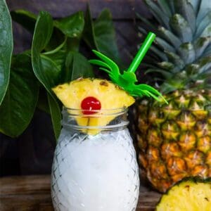 close up Pina Colada in a pineapple jar garnish with a pineapple slice. Fresh pineapple on background.