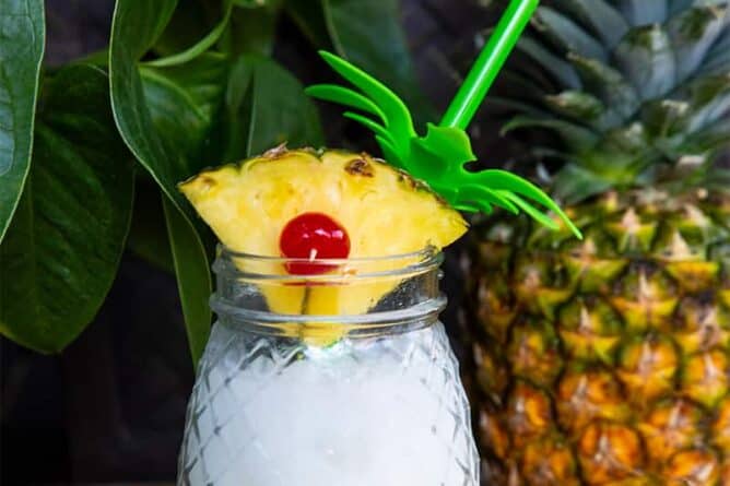 close up Pina Colada in a pineapple jar garnish with a pineapple slice. Fresh pineapple on background.