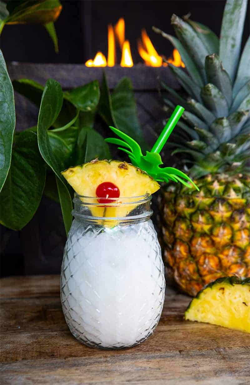 close up Pina Colada in a pineapple jar garnish with a pineapple slice. Fresh pineapple on background.