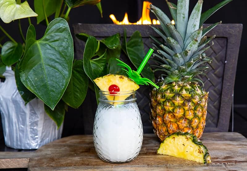 pina colada cocktail using a pineapple wedge as a garnish, with a large whole pineapple beside it 