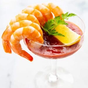 6 cocktail shrimp around a serving glass with Cocktail Sauce garnish with a slice of lemon and parsley leaves