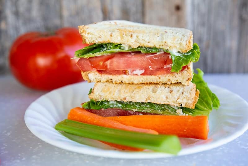 Classic Toasted Tomato Sandwich in a white plate. A large tomato on the background