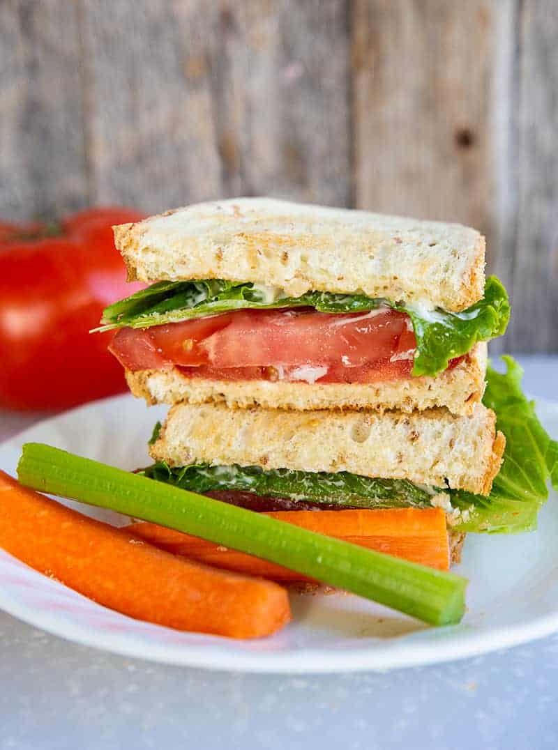 Classic Toasted Tomato Sandwich in a white plate. A large tomato on the background