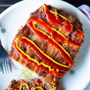 slice up Bacon Cheeseburger Meatloaf topped with cheese, mustard and ketchup in a white plate with fork
