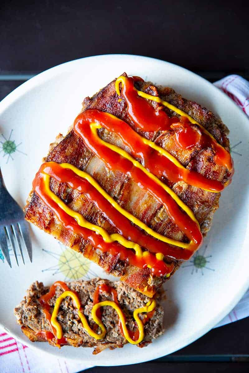 high angle shot of a slice up Bacon Cheeseburger Meatloaf topped with cheese, mustard and ketchup