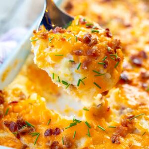 close up spoonful of Baked Cheesy Potato Casserole topped with chives and bacon