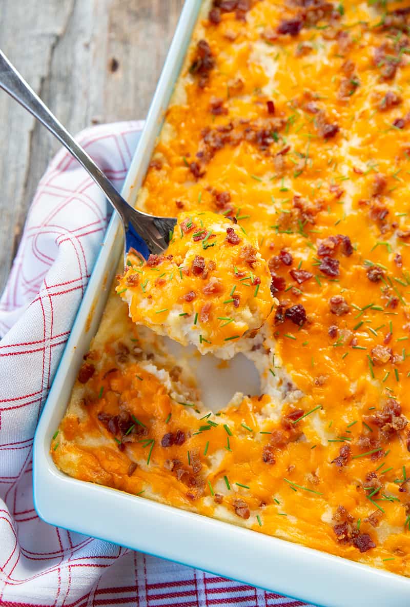 spoonful of Baked Cheesy Potato Casserole from a baking pan with kitchen cloth underneath