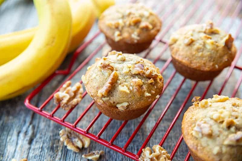 Banana Nut Muffins in red cooling rack, ripe bananas on its background