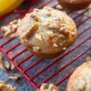 close up Banana Nut Muffins in red cooling rack, ripe bananas on its background