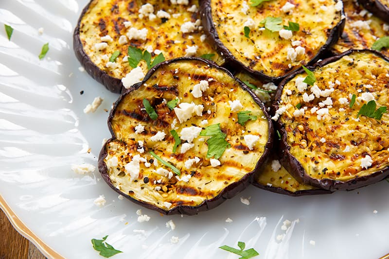 sliced Grilled Eggplant with some some feta cheese and parsley in a white plate