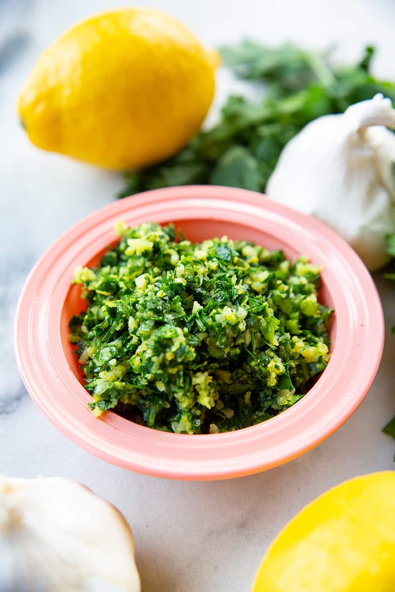 close up Classic Italian Gremolata in a pink saucer plate a, lemon and garlic head on background