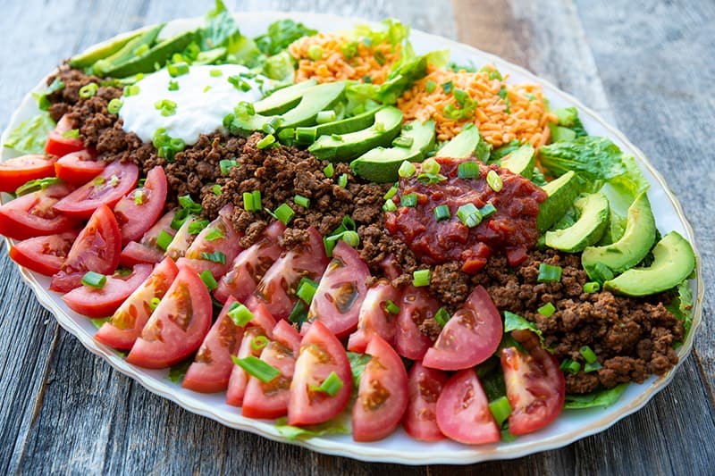 a platter full of Ground Beef Taco Salad topped with fritos and chopped green onions