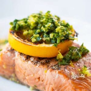 close up a piece of grilled salmon fillet with a slice of lemon and gremolata on top