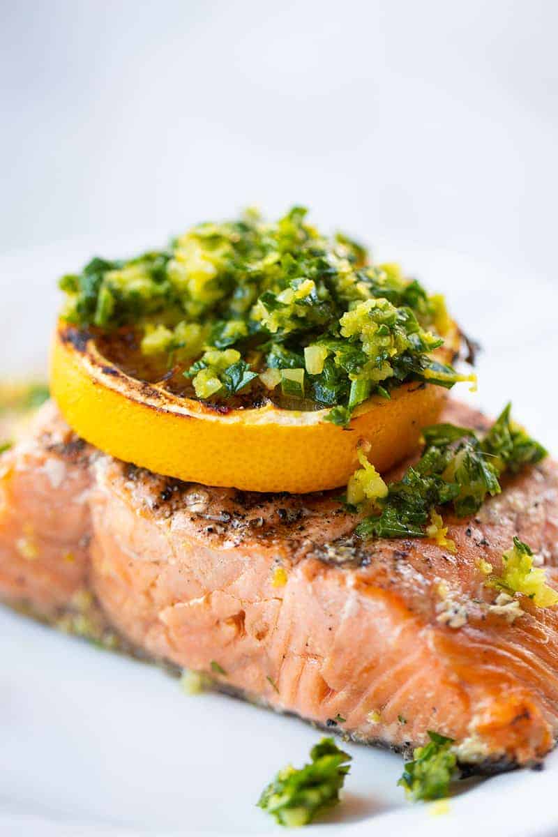 close up a piece of grilled salmon fillet with a slice of lemon and gremolata on top