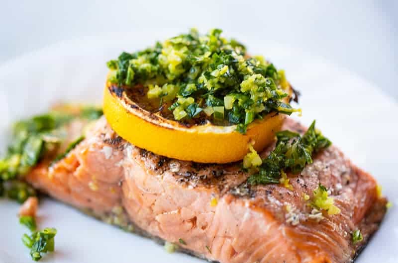 a piece of grilled salmon fillet with a slice of lemon and gremolata on top