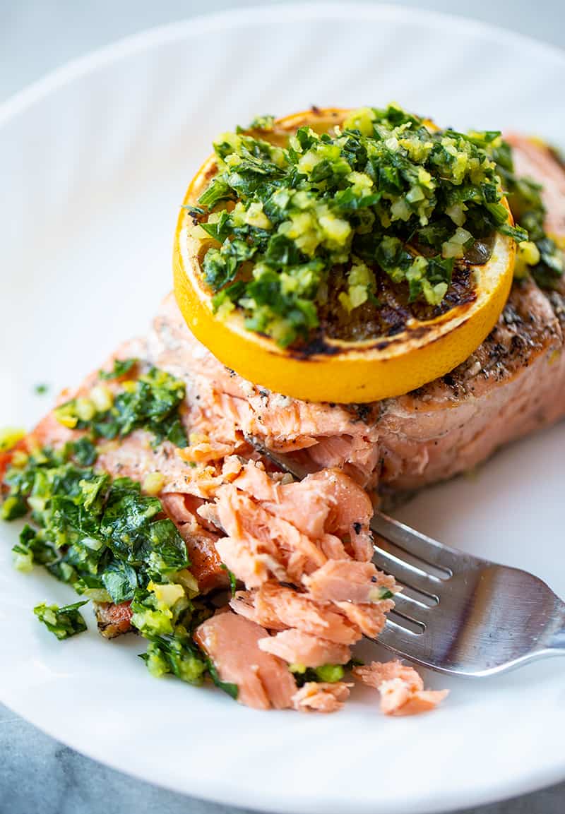 using a fork in flaking a slice of grilled salmon fillet with a slice of lemon and gremolata on top