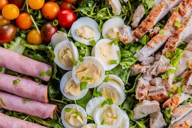 close up plate of Classic Cobb Salad - romaine lettuce, watercress, sliced hard boiled eggs, cherry tomatoes and all other ingredients