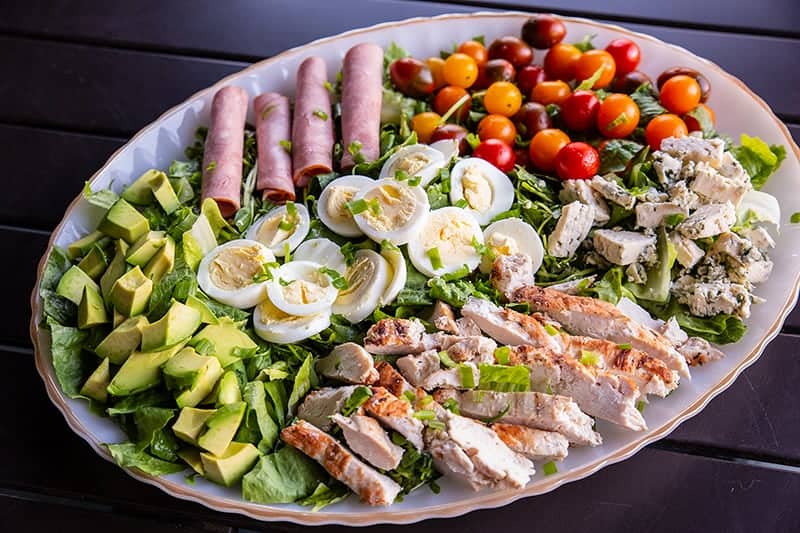 a plate of Classic Cobb Salad - romaine lettuce, watercress, sliced hard boiled eggs, cherry tomatoes and all other ingredients