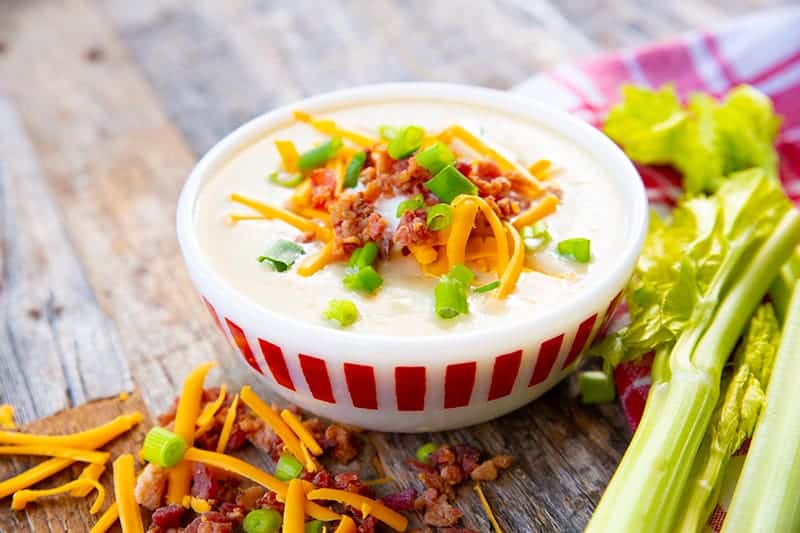 white soup bowl with Cream of Celery Soup topped with shredded cheese, bacon bits and green onions