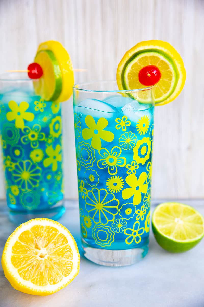 close up Electric Lemonade cocktails side by side in vintage flower glasses garnish with lemon and lime 