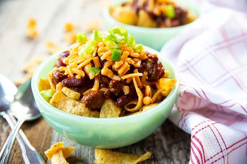 mint green bowl with Frito Pie loaded with chili, shredded cheddar cheese and thinly sliced green onions