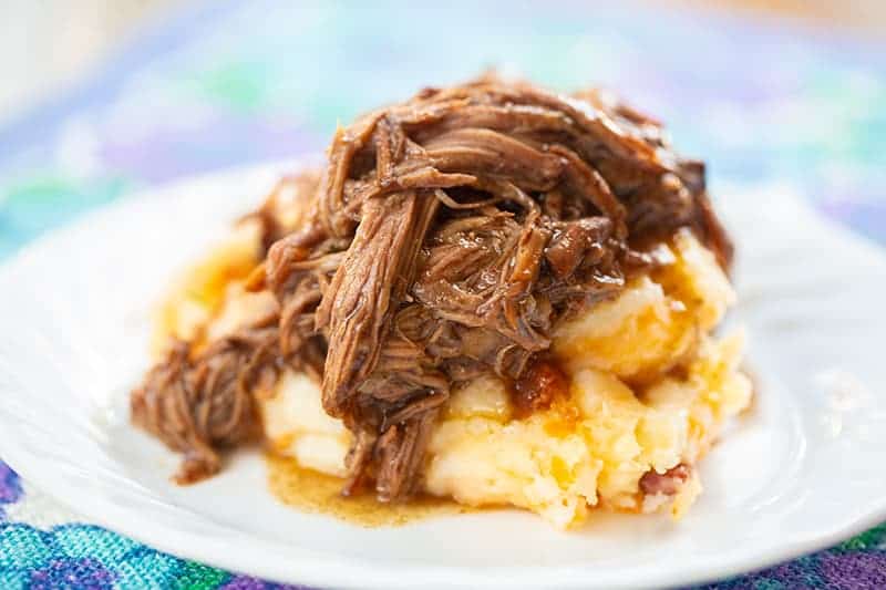 3 Ingredient Shredded Beef with mashed potatoes on a white serving plate, blue floral tablecloth underneath