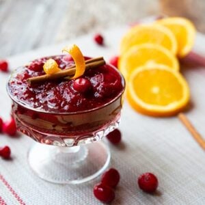 Homemade Cranberry Sauce in a glass. Some slices of orange, cinnamon sticks and cranberries on background