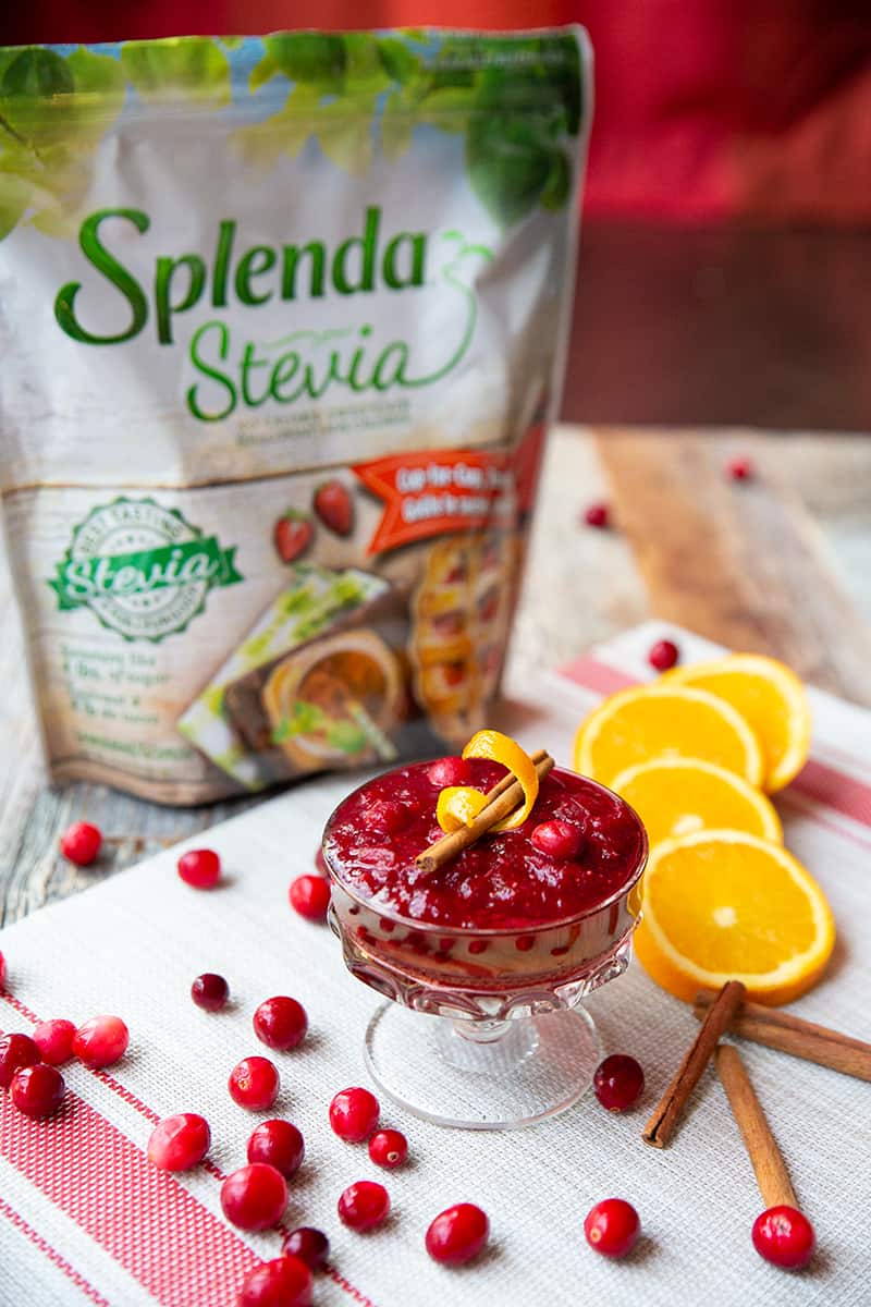 close up Homemade Cranberry Sauce in a glass. A pack of Splenda Stevia, some slices of orange, cinnamon sticks and cranberries on background