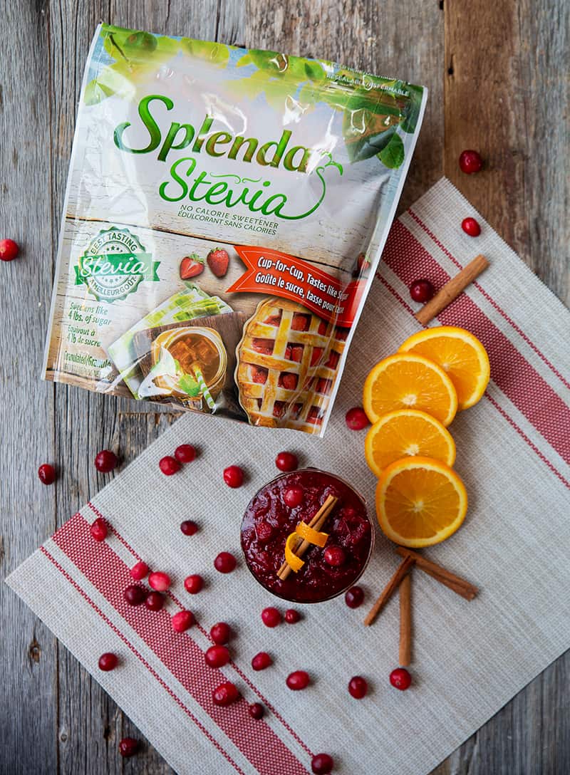 Homemade Cranberry Sauce in a glass. Slices of orange, cinnamon sticks, cranberries and a pack of Splenda Stevia on background.