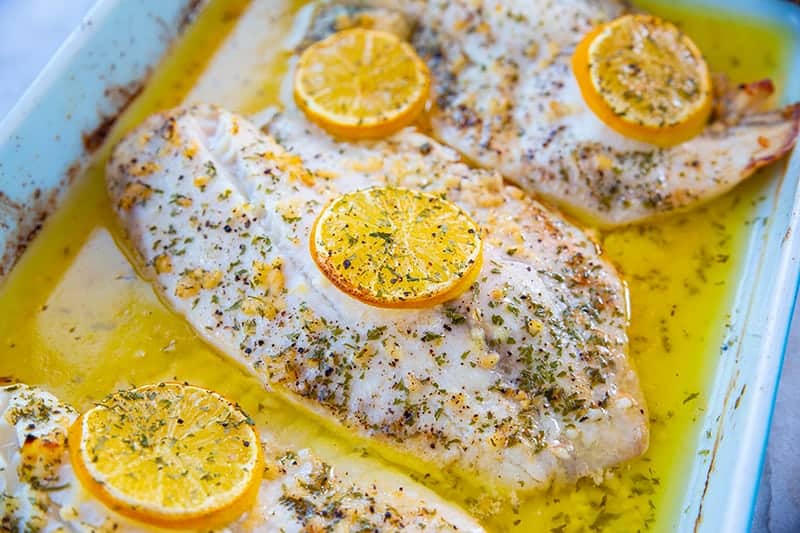 butter poached lemon garlic tilapia in baking dish, garnish with lemon slices