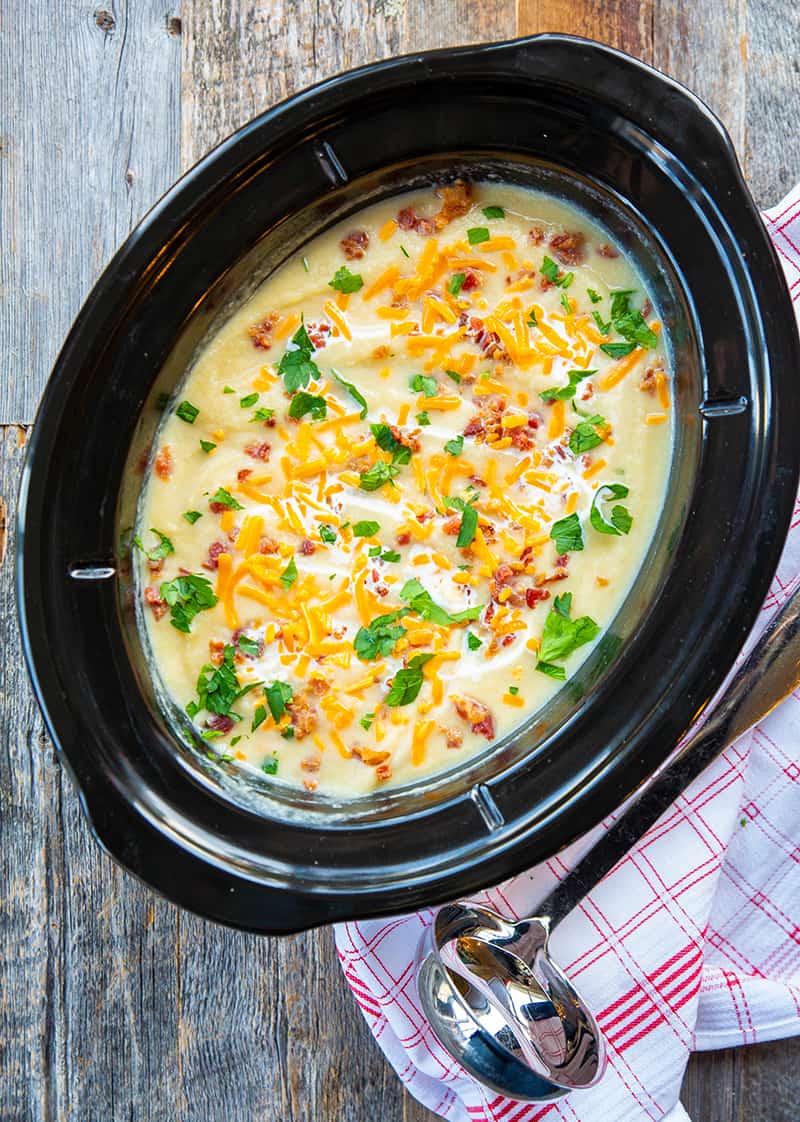Creamy Cauliflower Leek Soup in a large black slow cooker with deep soup spoon on its side