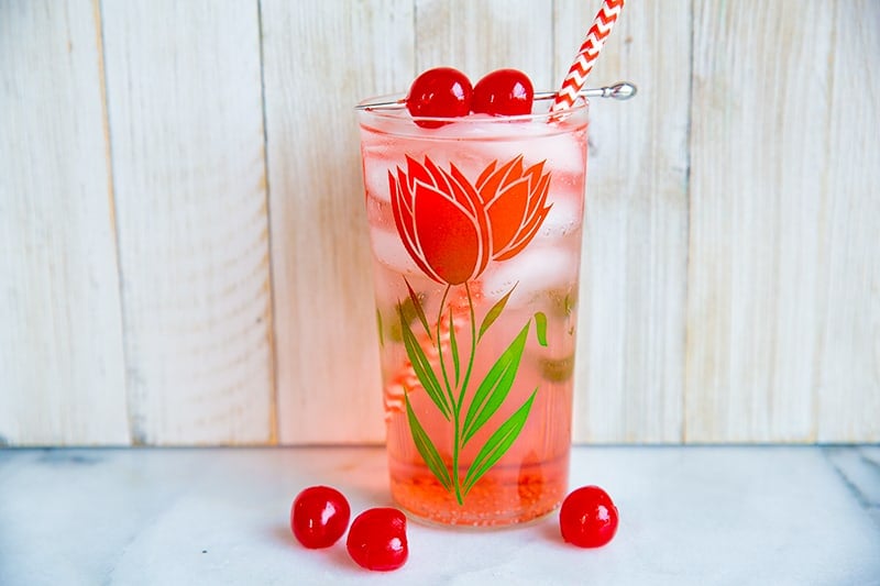 Dirty Shirley Cocktail in a glass with flower design, garnish with cherries