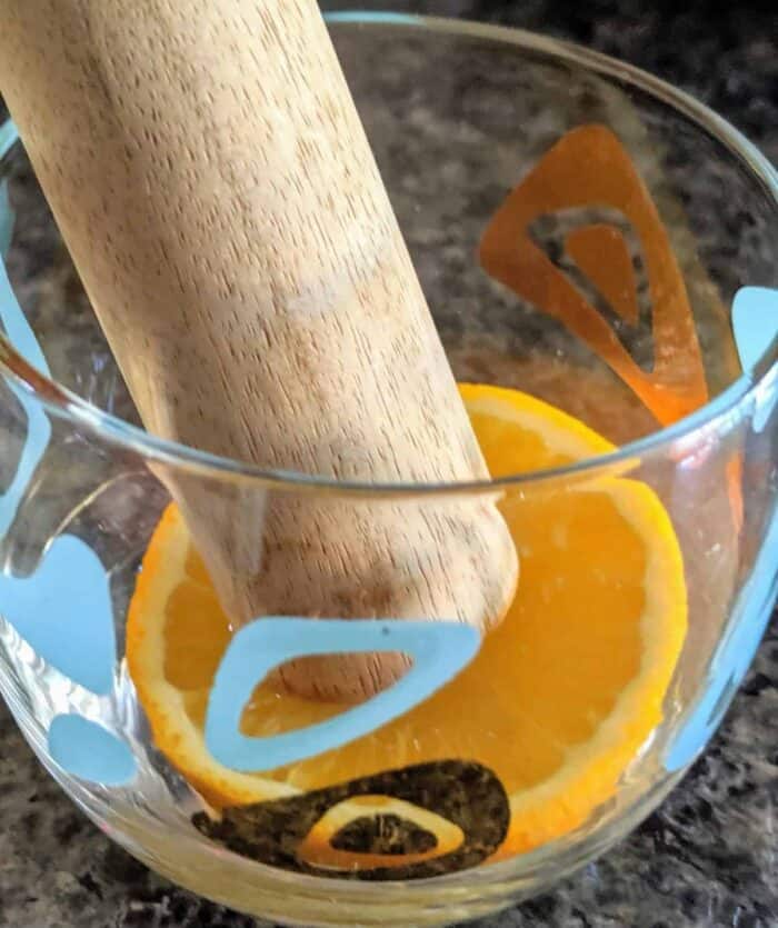 close up Muddling an Orange slice in a glass using a Muddler