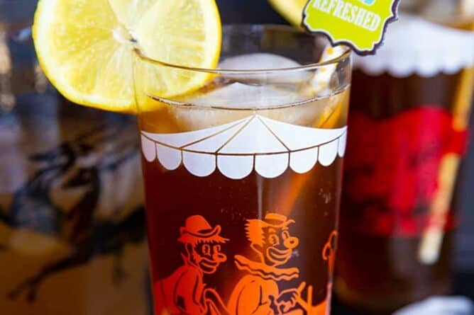 close up glass of Long Island Iced Tea garnish with slice of lemon, a pitcher and another glass on its background