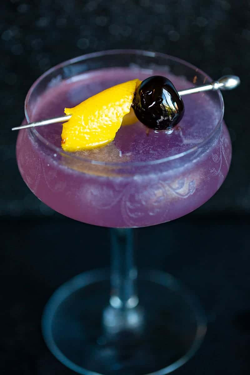 close up Aviation Cocktail in a coup glass with olive and a slice of orange