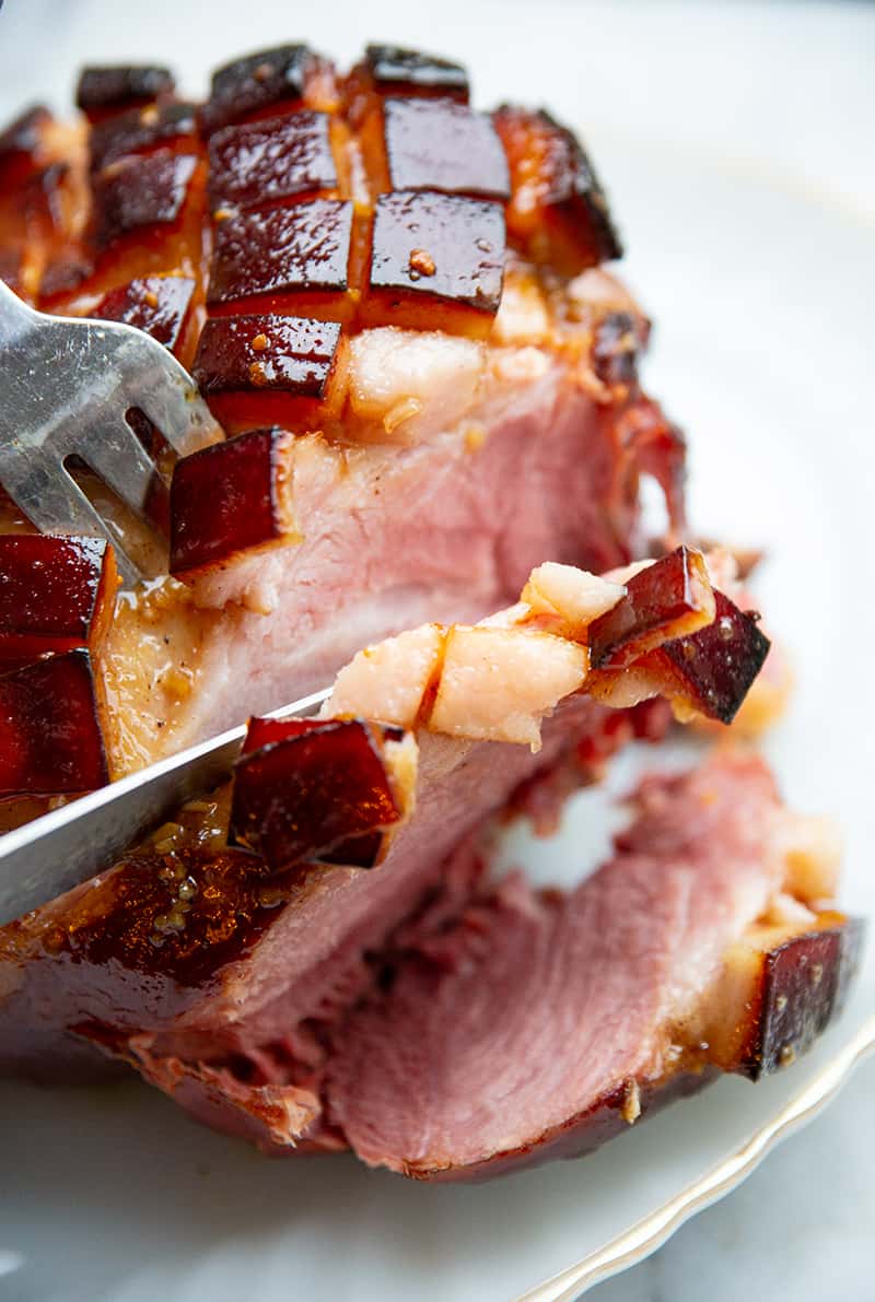 close up slicing Brown Sugar Glazed Baked Picnic Ham using fork and ham knife