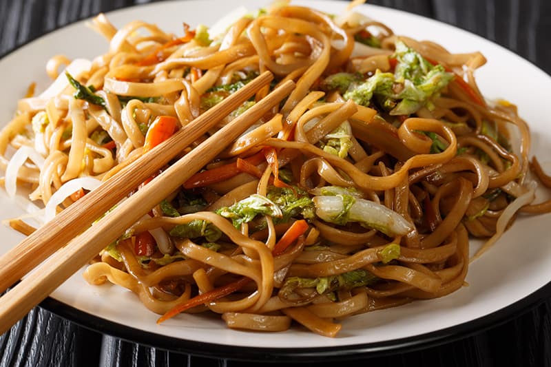 Pork Chow Mein in a white plate with chopsticks on top - Chow Mein vs Lo Mein