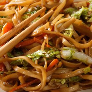 close up Pork Chow Mein in a white plate with chopsticks on top - Chow Mein vs Lo Mein