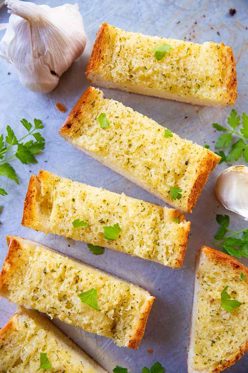 Classic Garlic Bread slices on a baking sheet with garlic bulb and dried parsley