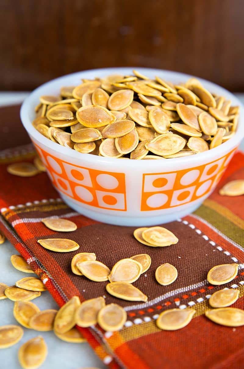 close up red orange kitchen cloth underneath a white bowl of Salty Crispy Roasted Pumpkin Seeds