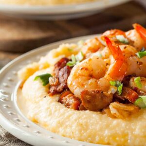 close up kitchen towel underneath white serving plate with Grits topped with shrimp and chopped spring onions