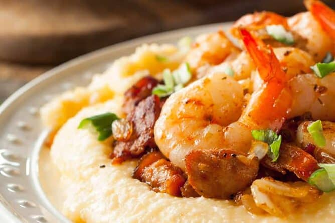 close up kitchen towel underneath white serving plate with Grits topped with shrimp and chopped spring onions