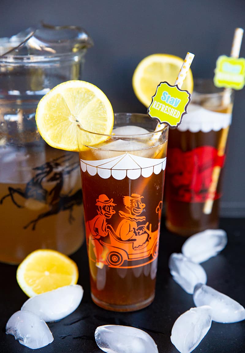 close up glass of Long Island Iced Tea garnish with slice of lemon, a pitcher and another glass on its background