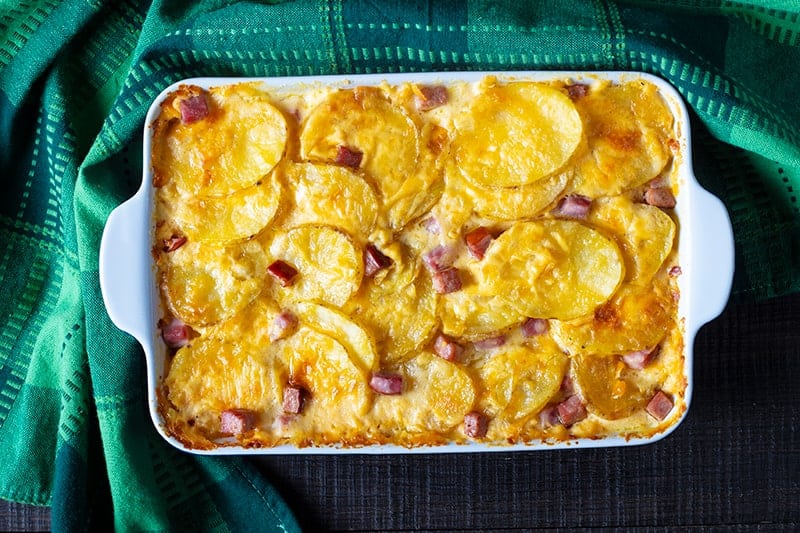 Scalloped Potatoes and Ham in a white casserole dish with green tablecloth underneath