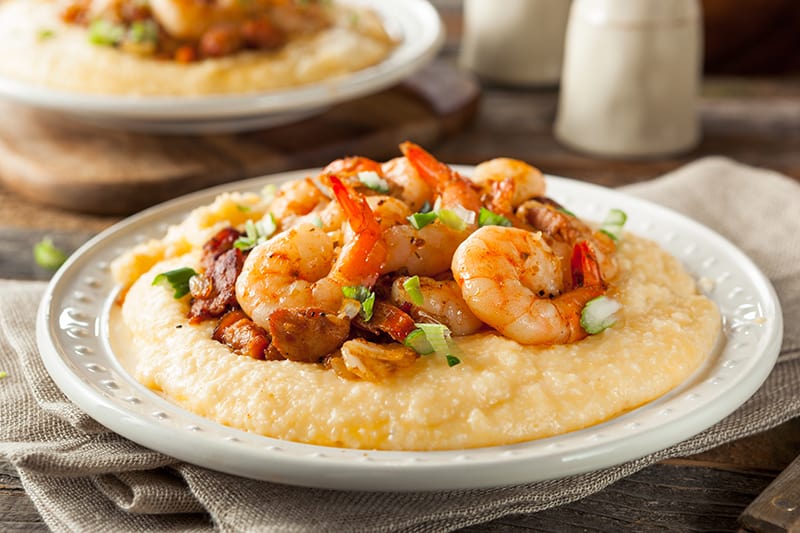 kitchen towel underneath white serving plate with Grits topped with shrimp and chopped spring onions