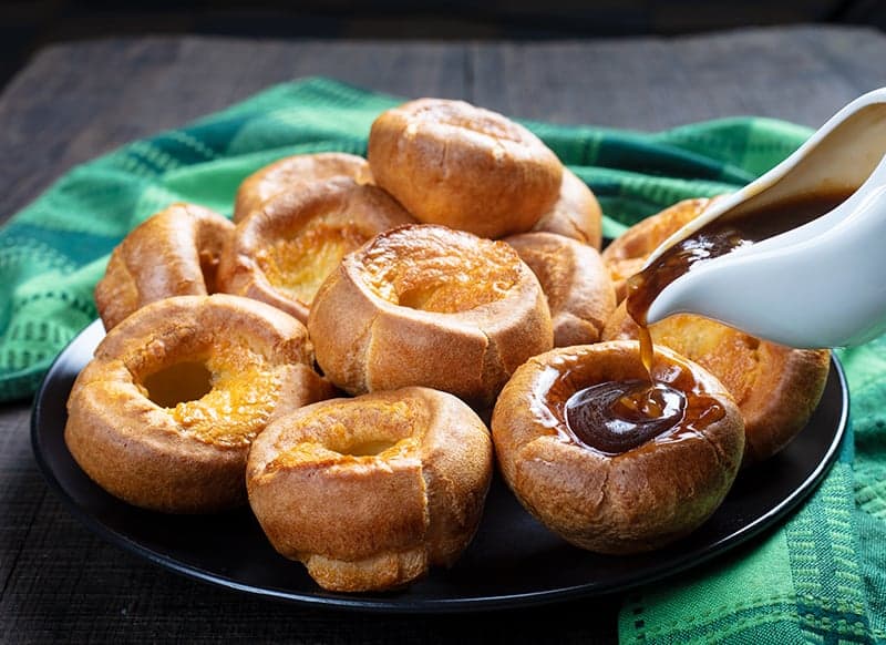 Traditional Yorkshire Pudding on a black serving plate with brown gravy, a green tablecloth underneath