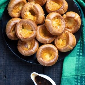 Traditional Yorkshire Pudding on a black serving plate with brown gravy, a green tablecloth underneath